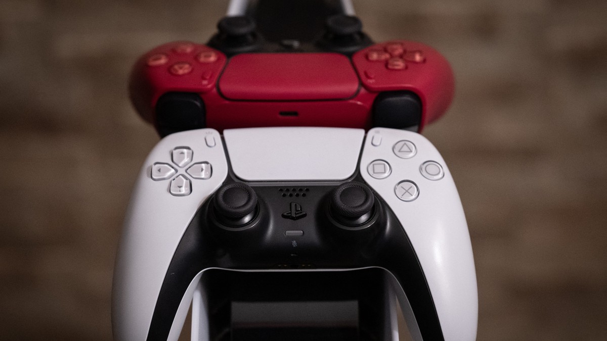 Două controllere de PlayStation 5, unul alb, unul roșu, așezate pe un stativ.
