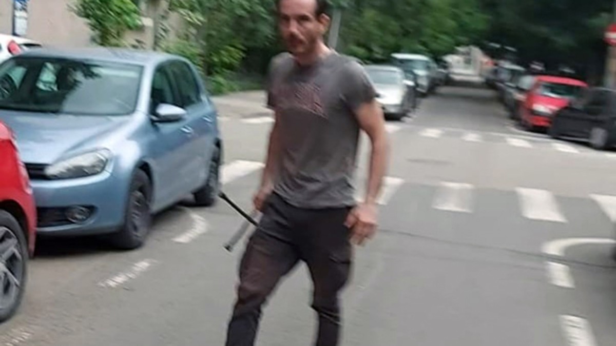 un bărbat cu un levier în mână pe o stradă, în spate se văd mai multe mașini parcate și altele în trafic