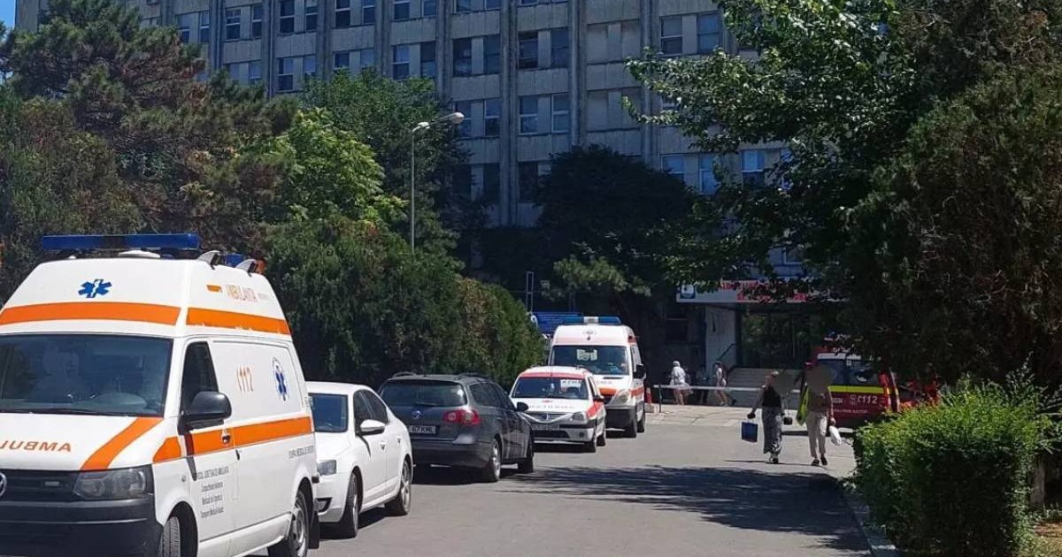 Spitalul Clinic de Urgență Constanța, vazut de afara, se observa ambulante, masini, oameni care merg spre intrarea spitalului, umbrit de mai multi pomi verzi, vara