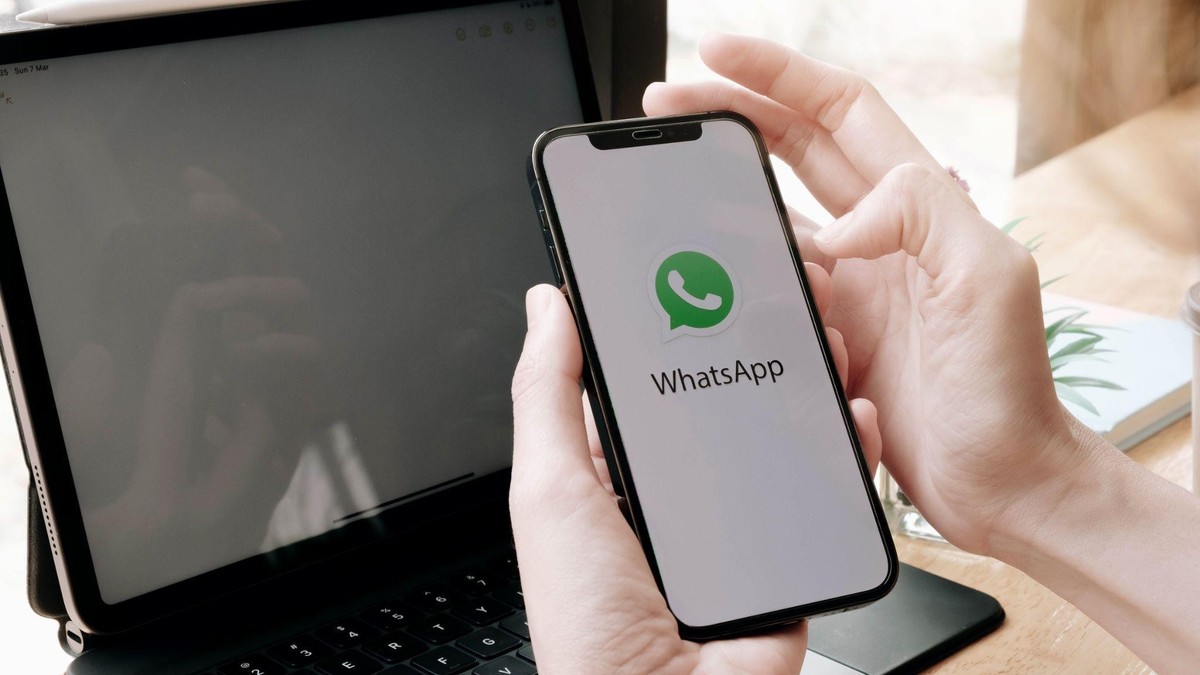 Maine de barbat care tin un telefon deschis pe Whatsapp in fata unei laptop