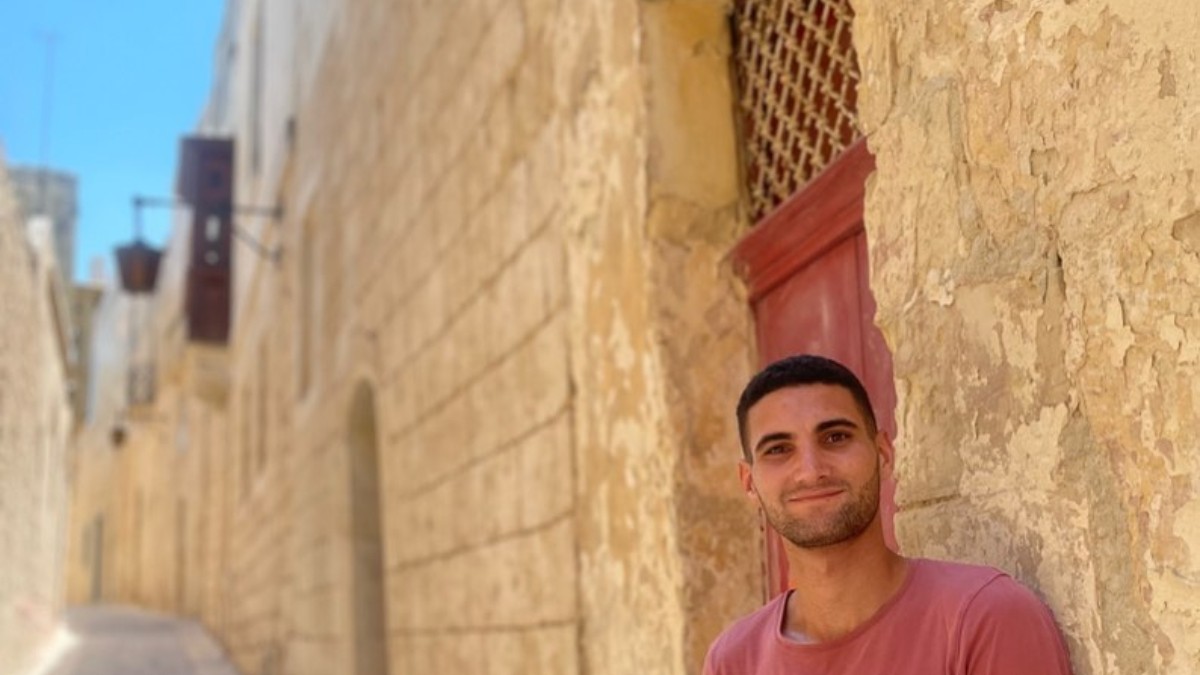 Un tânăr turist pe străzile din Malta, bărbatul are părul negru, tuns scurt și poartă un tricou roșu