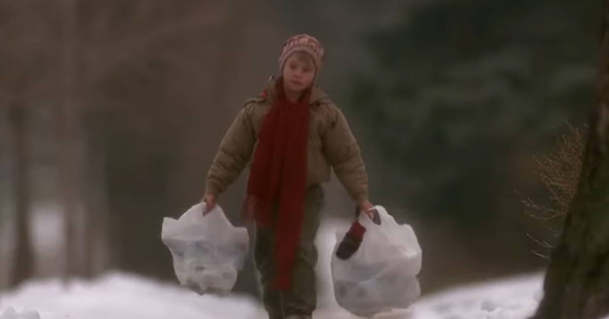 Captura video din filmul Singur Acasa, 1990, când Kevin McCallister, interpretat de Macaulay Culkin, cara doua plase de cumparaturi pline, albe, cate una in fiecare mana, este immbracat in geaca groasa maro deschis, are un fular rosu lung, pantaloni kaki si caciula, pe o alee, iarna, zapada pe marginea drumului, in spate se vad brazi verzi si pomi fara frunze