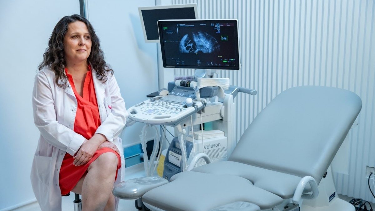 O femeie bruneta, in rochie rosie, imbracata in halat alb, sta pe scaun intr-un cabinet de ginecologie. FIV, ovocite, fertilitate