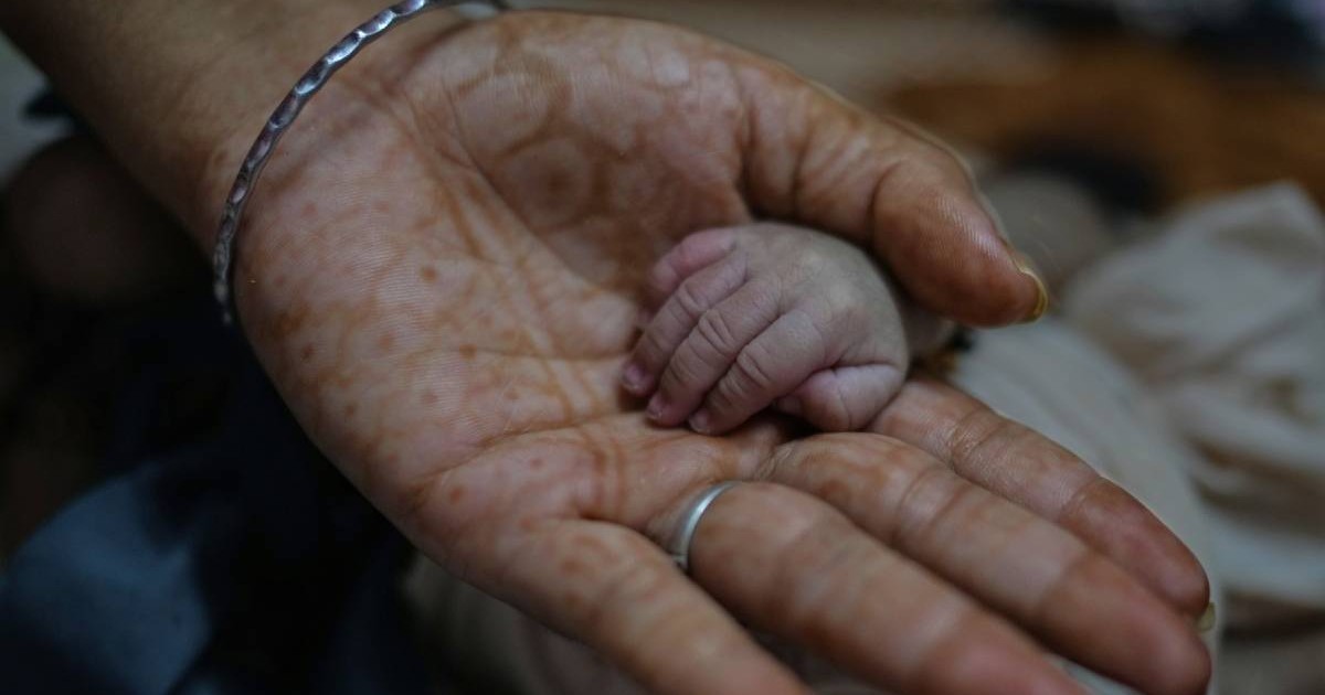 Cadru strâns cu mana unei femei din India, cu tatuaje Henna, cu un inel pe un deget, care ține mana mică a unui nou-născut