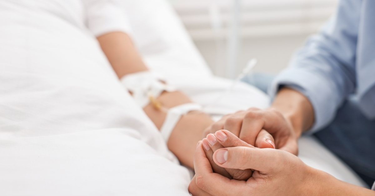 Un cadru medical ține de mână un bolnav aflat în spital, pe patul de moarte