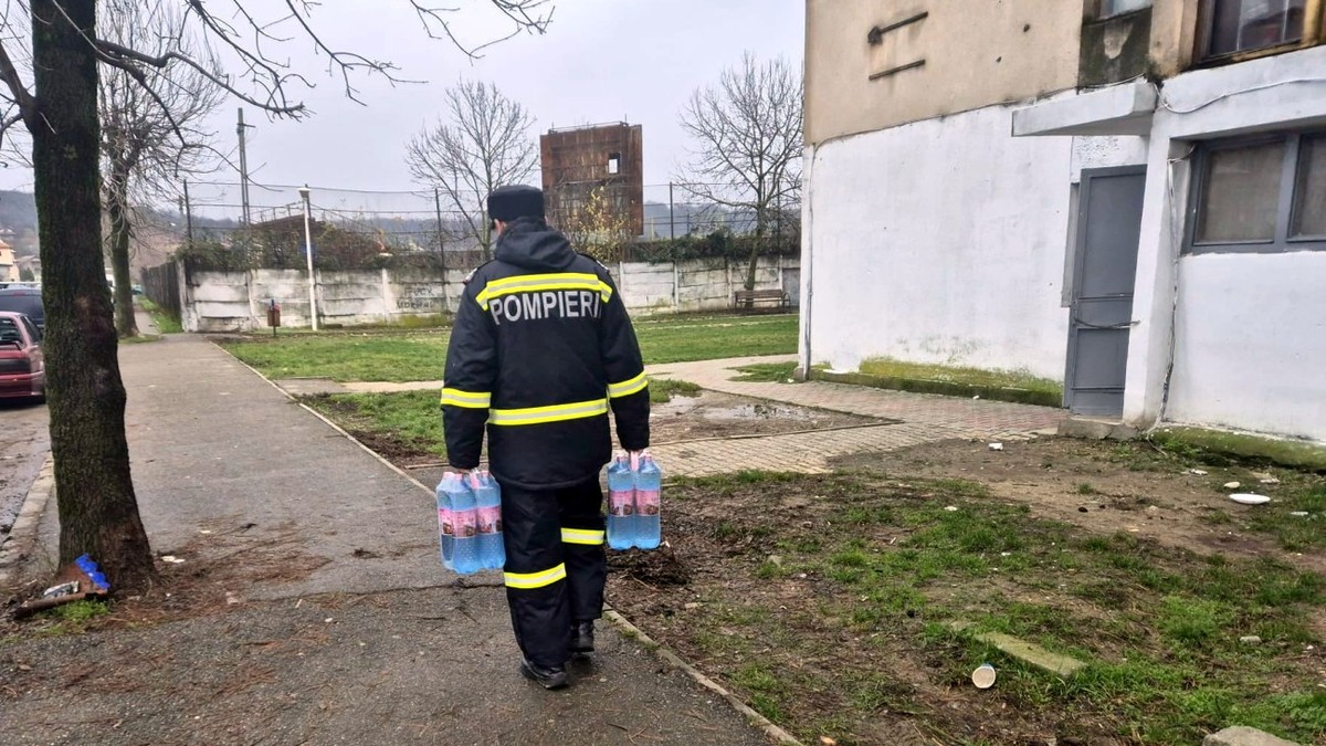 Imagine cu un pompier care duce sticle cu apă locuitorilor care nu mai au apă la robinet
