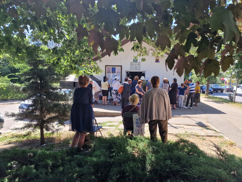 Oamenii asistă la slujbă instalați la umbră, pe scaune rabatabile