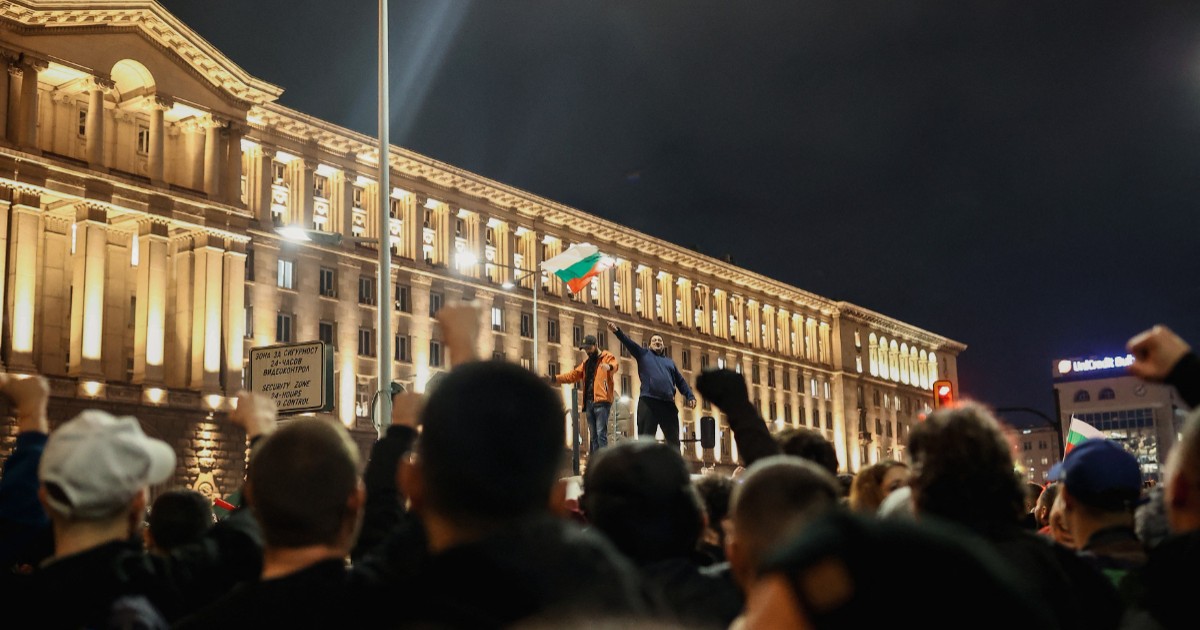Protestele violente din Bulgaria, doi oameni s-au urcat pe o dubită în Sofia și flutură steagul Bulgariei, în timp ce restul manifestanților scandează lângă ei