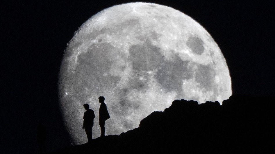 Luna în creștere răsare în spatele unor oameni aflați aproape de vârful lui Arthur's Seat din Parcul Holyrood, Edinburgh. Sursă foto: Hepta.