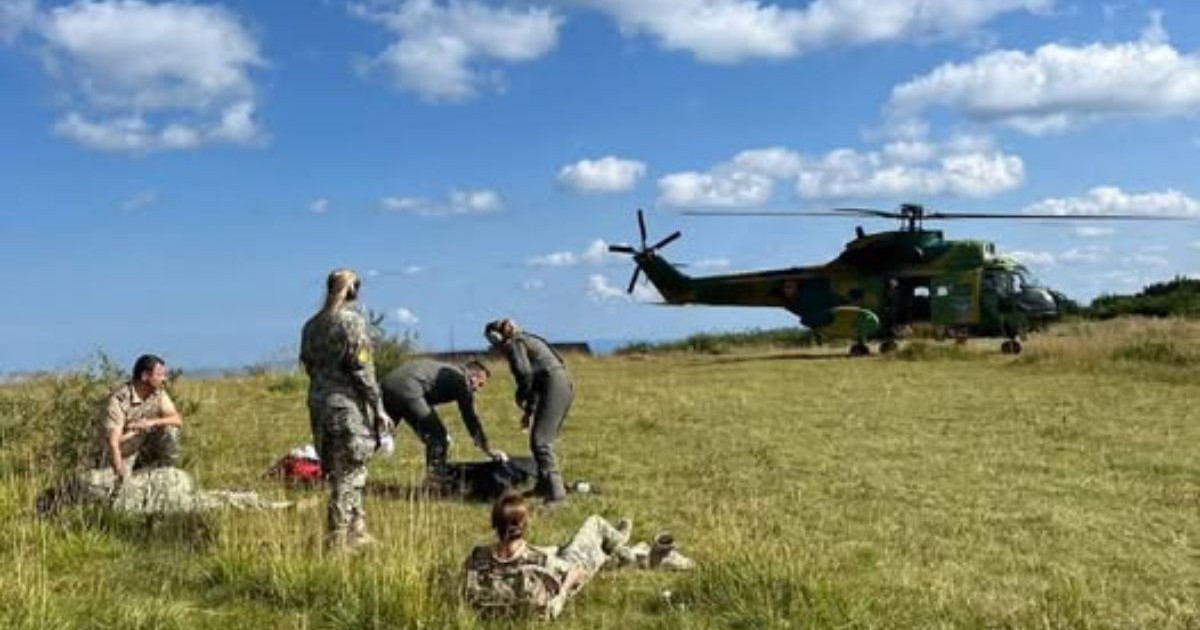 In imagine un elicopter al MApN aterizat pe o zona cu iarba, se vad 5 persoane, unii militari ai fortelor aeriene romane