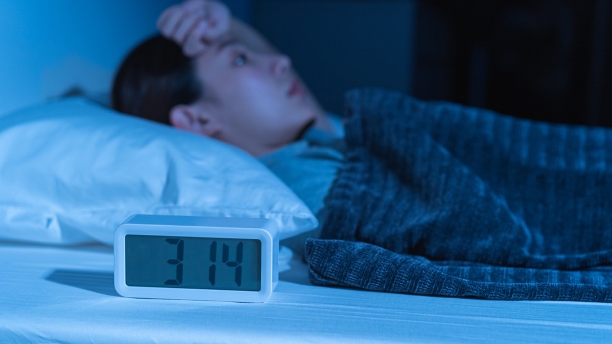 Cum previi şi tratezi insomnia - O femeie sta in pat cu ochii deschisi, uitandu-se in tavan, desi ceasul de langa ea arată ca e trecut de ora 3 dimineata