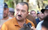 Un bărbat cu mustață vorbind în fața mai multor microfoane, înconjurat de oameni și jurnaliști
