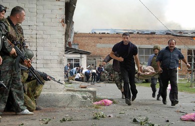 Ossetian volunteers carry injured pupil as soldiers of special police forces keep behind a wall in the school garden during the attack operation in the town of Beslan, North Ossetia, 03 September 2004. One hundred and fifty-eight children have been taken to hospital here after special forces on Friday stormed a Russian school where militants were holding hundreds hostage, the regional president told Moscow Echo radio.,Image: 15935409, License: Rights-managed, Restrictions: , Model Release: no