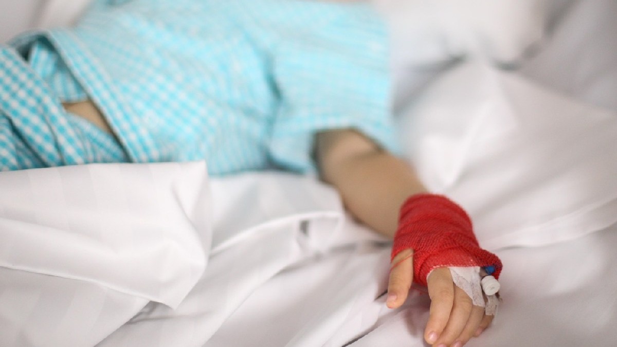 o canulă pe mâna unei fetițe bolnave, care stă pe un pat, într-un spital