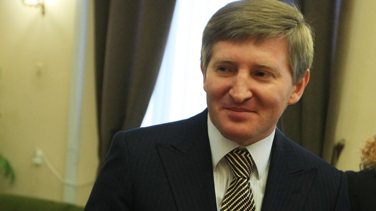 Rinat Ahmetov într-un costum negru și cămașă albă, în timp ce zâmbește