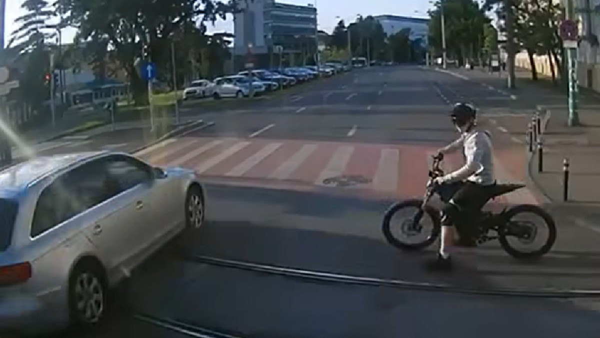 Un copil încearcă să traverseze cu bicicleta pe la o trecere de pietoni și se îndreaptă exact spre o mașină albă care a oprit în ultimul moment