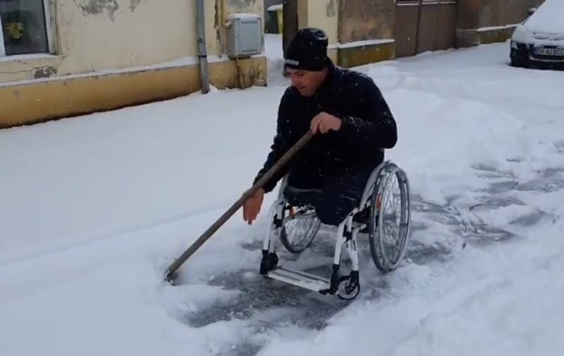 Exemplu de atitudine civică: un bărbat în scaun cu rotile, filmat în timp ce deszăpezește trotuarul