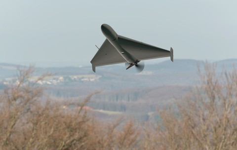 O dronă militară gri în formă de aripă triunghiulară zboară la joasă altitudine deasupra unei zone împădurite și a unui peisaj deluros. Poză cu caracter ilustrativ. Foto: Shutterstock