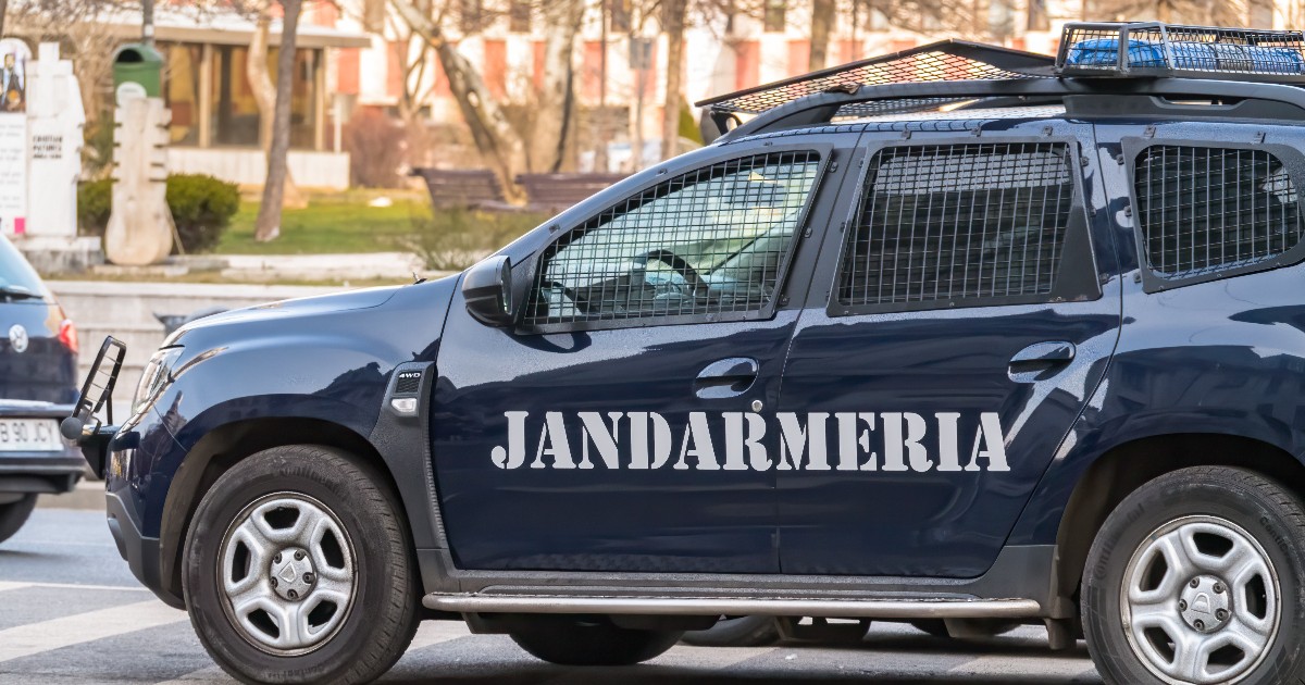 O autospecială a Jandarmeriei este surprinsă staționând pe o stradă urbană, cu inscripția instituției vizibilă pe portieră. Vehiculul este dotat cu grilaje de protecție și echipamente specifice intervențiilor de ordine publică.