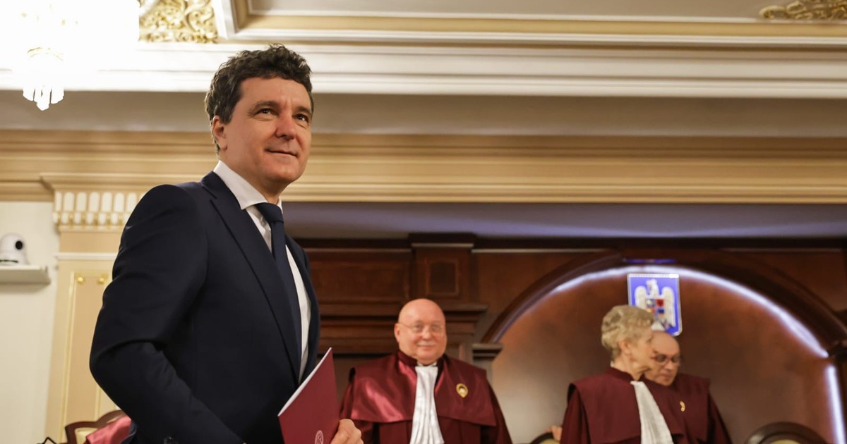 Nicușor Dan ține o mapă cu documente în mâini și zâmbește, în fundal se observă judecătorii CCR îmbrăcați în robe.