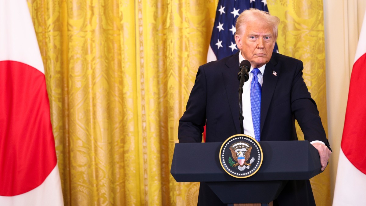 Donald Trump, îmbrăcat într-un costum albastru închis, cu cămașă albă și cravată albastru deschis, stă cu mâinile pe un pupitru care are un microfon. În spatele lui e o cortină galbenă și steagul americii.