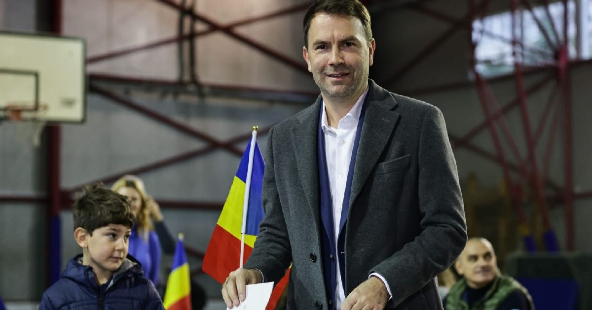 Fotografie cu Cătălin Drulă îmbrăcat într-un costum gri care votează într-o sală de sport