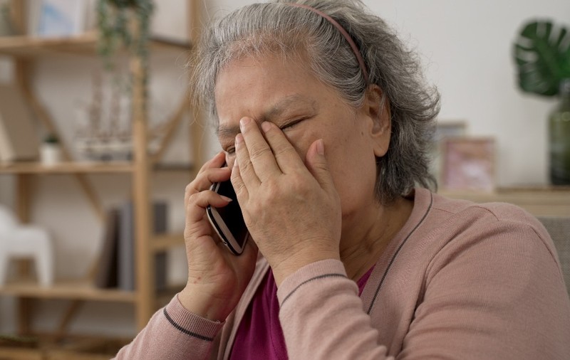 O femeie bătrână care vorbește la telefon și ține o mână pe frunte