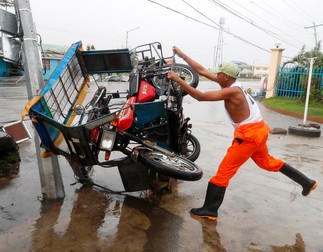 Un filipinez își ține cu greu motocicletă răsturnată de taifun FOTO: EPA-EFE/FRANCIS R. MALASIG
