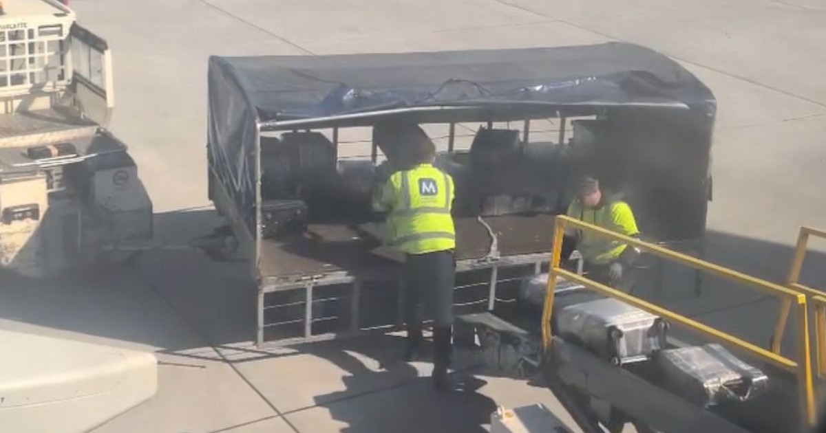 doi angajați ai aeroportului internațional cluj napoca, îmbrăcați în jachete verzi fosforescente cu litera M pe spate, scrisă cu albastru, aranjează trolere într-un vehicul de transport