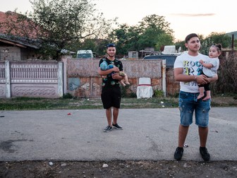 Doi tați stau cu copiii în timp ce nevestele lor dansează la botez. Corcova, Mehedinți, august 2023