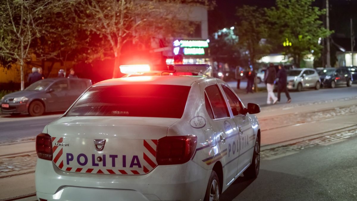 Mașină de Poliție, cu girofarul pornit, de culoare roșie, pe o stradă, pe timp de noapte