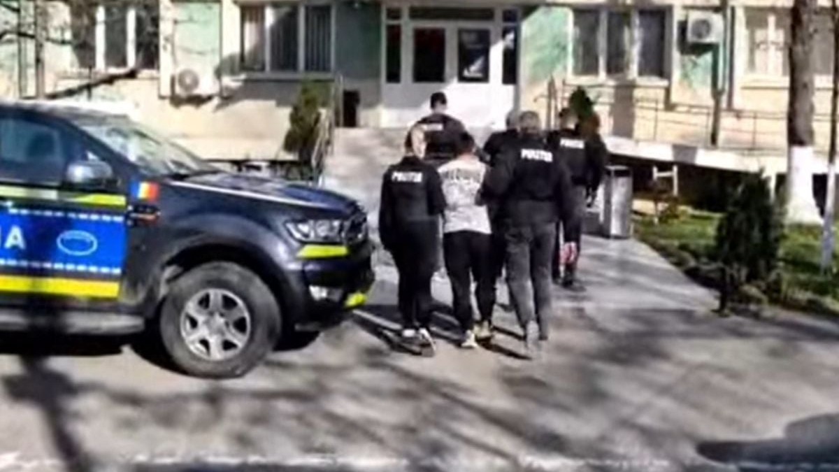 Cei doi suspecți reținuți, escortați de polițiști, în fața sediului Poliției din Slatina, cu o mașină de Poliție în față
