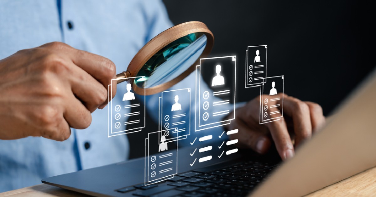 Un barbat cu o lupa in mana, in fata unui laptop - Sugereaza - Recrutare digitală și procesul de screening HR formular online și profiluri de candidați.