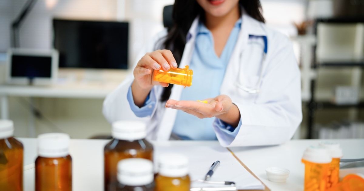 O femeie bruneta, cu parul lung, imbracata inhalat alb pune dintr-un flacon de medicamente un medicament in palma, pe masa de lucru are mai multe flacoane cu medicamente. Terapie experimentala cancer pancreatic,oncologi romani. Foto Shutterstock