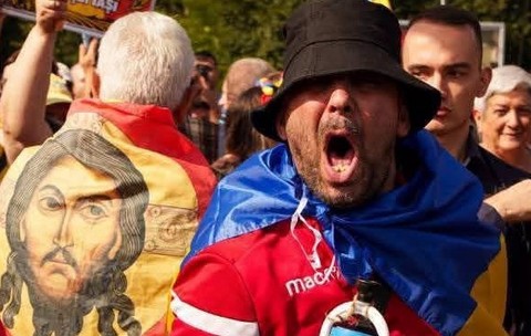 O imagine cu fața lui Isus pe un steag purtat pe spate de un protestatar, langa un al protestatar care tip la protestul fermierilor din Piața Victoriei, de pe 15 septembrie