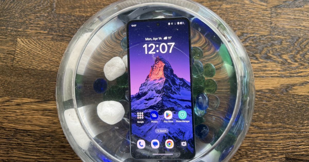 Un smartphone OPPO Reno13 F 5G, scufundat într-un bol plin cu apă și pietre colorate.