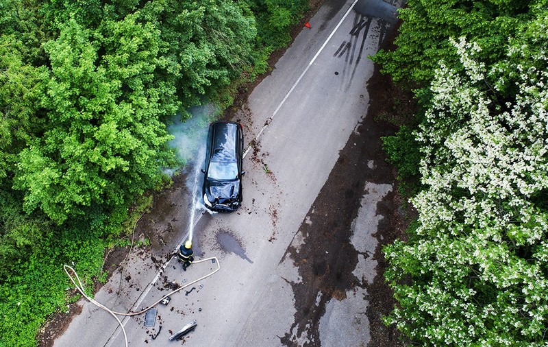 Pompieri care sting un incendiu al unei mașini accidentate