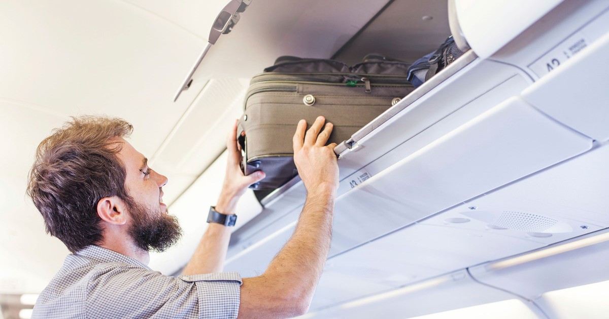 Un bărbat introduce un troller în spațiu de bagaje din interiorul unui avion.