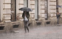 O persoană adăpostindu-se sub o umbrelă cu buline în timp ce merge pe trotuar pe o ploaie torențială, lângă fațada unei clădiri istorice.