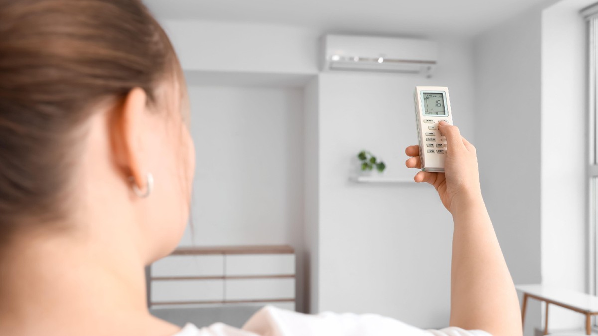 O persoană care reglează un aparat de aer condiționat cu ajutorul unei telecomenzi
