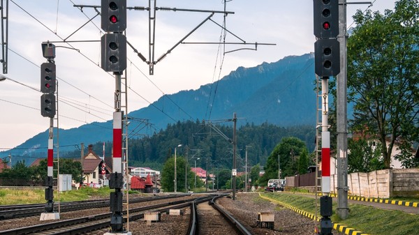 Trei linii de cale ferată într-o gară dintr-o zonă montană din România, luminile roșii de semnalizare sunt aprinse