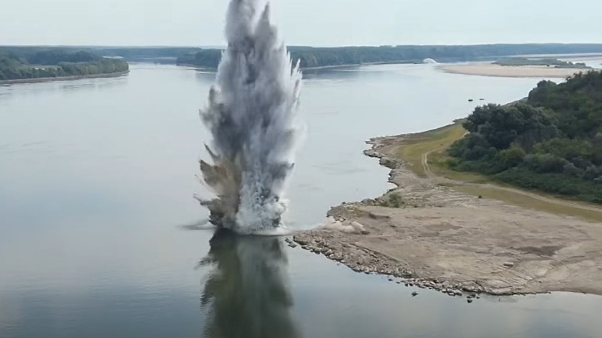 Imaginea surprinde o explozie puternică în apă lângă malul unui fluviu, aruncând o coloană uriașă de apă, praf și resturi în aer.