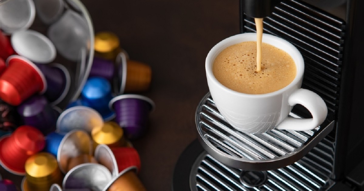 Cât de sănătoase sunt cafelele obţinute din capsule - Imagine cu un espressor din care curge cafea intr-o ceaşcă, alături de capsule de cafea