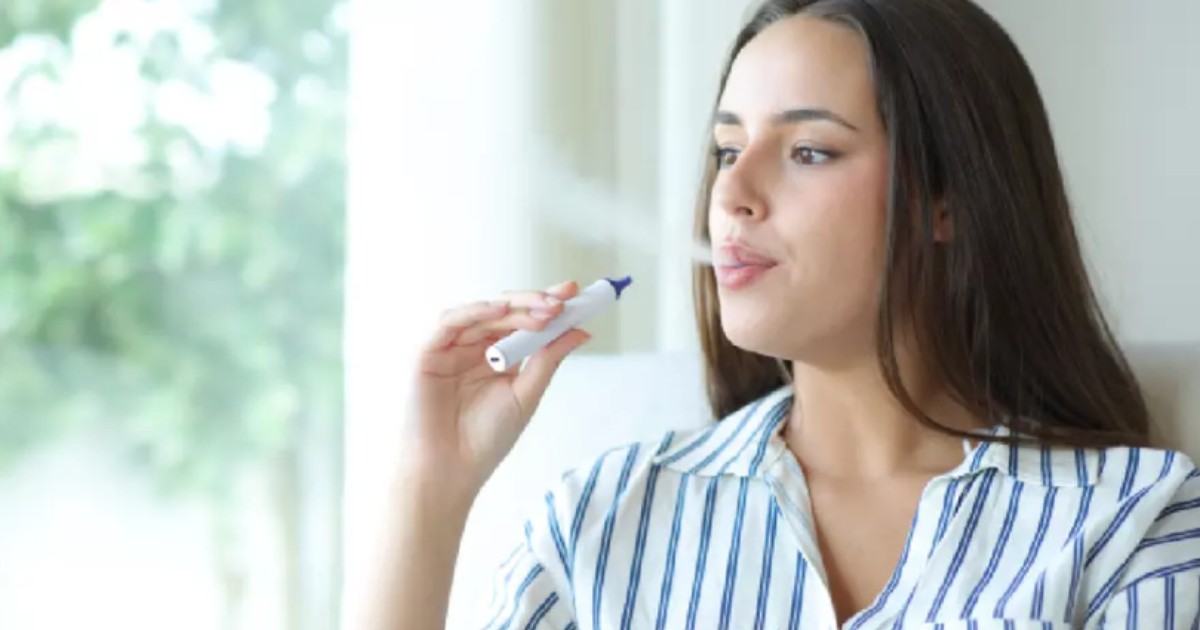 O tânără îmbrăcată în cămașă albă cu dungi albastre care vapează