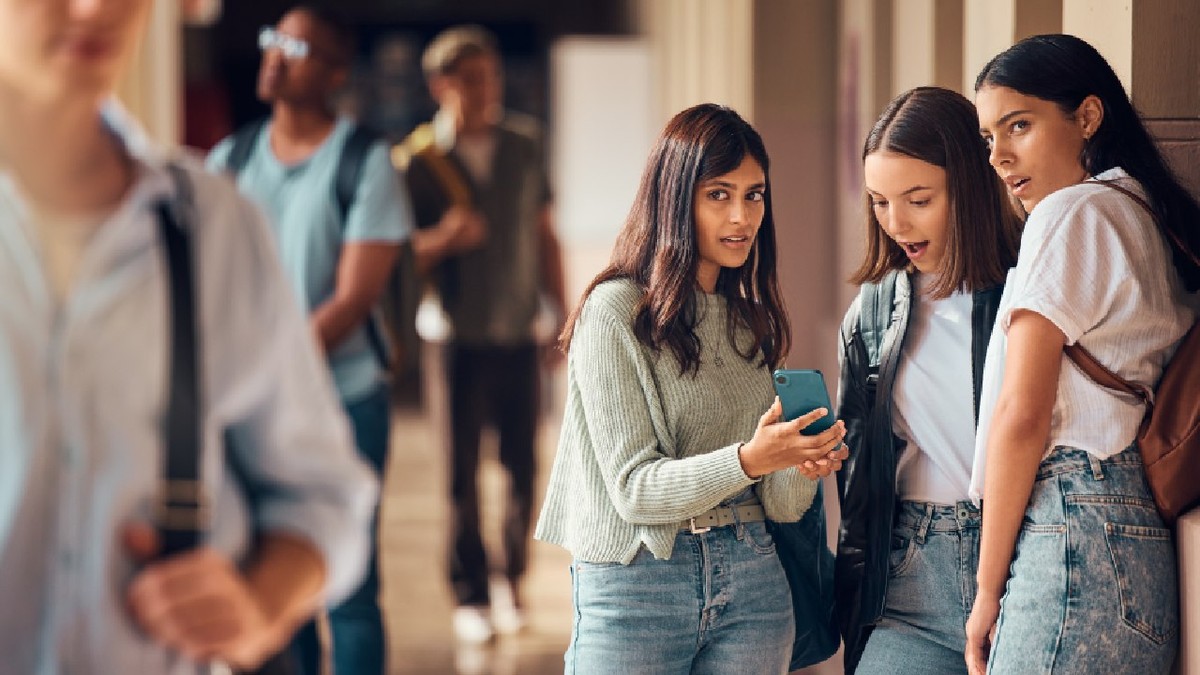 Un grup de adolescente pe holul unui liceu, se uita la un telefon mobil