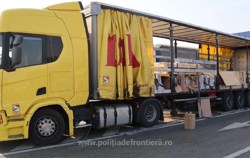 Un camion galben cu prelata de la remorca data la o parte, se vad mai multe cutii si paleti in remorca