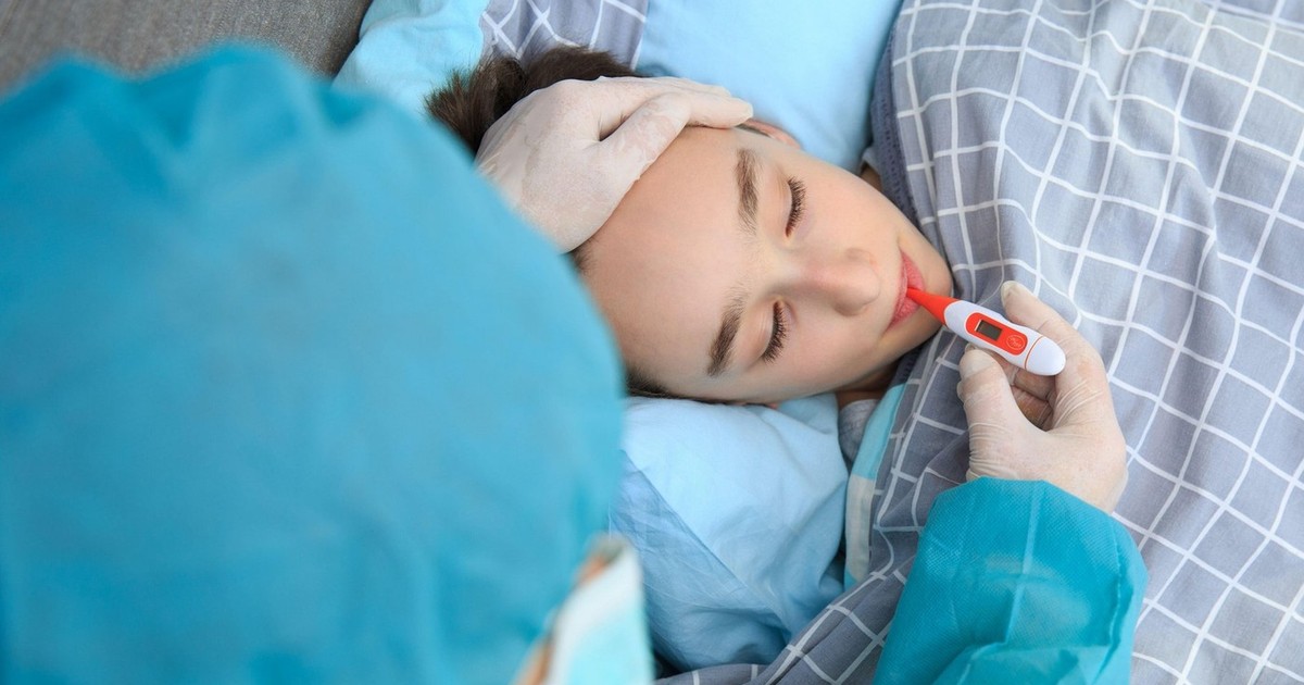 Un băiat bolnav stă întins pe pat și i se ia temperatura cu un termometru. În România a fost declarată stare de urgență epidemiologică din cauza gripei