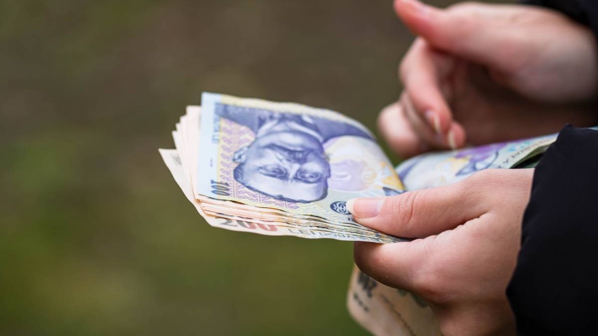 O femeie româncă care numără mai multe hârtii de 100 de lei, îi ține în mână