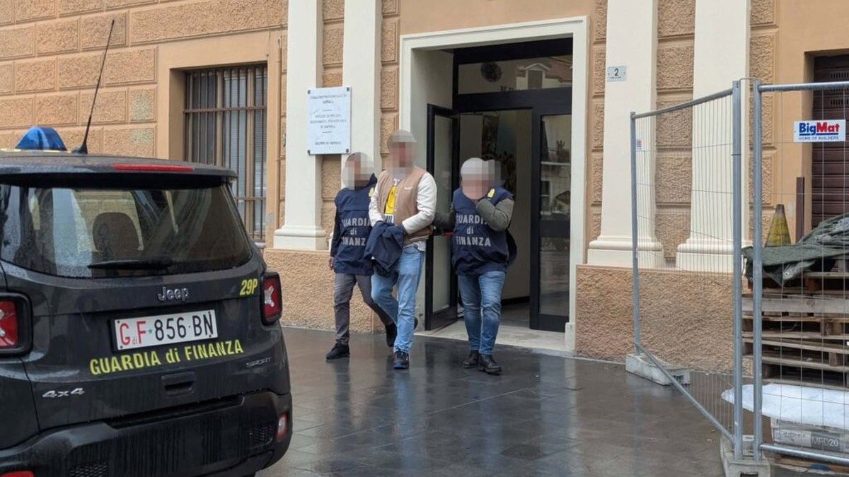 Un șofer român de TIR cu cătușe la mâini ascunse de o geacă (mijloc) este încadrat de doi polițiști, toți trei având fețele burate, Italia, 2 februarie 2026