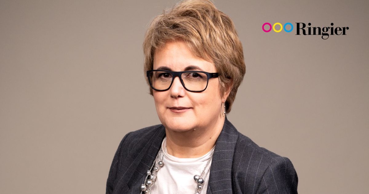 Mădălina Rădulescu, îmbrăcată cu o bluză albă și un sacou gri, cu ochelari de vedere de culoare neagră
